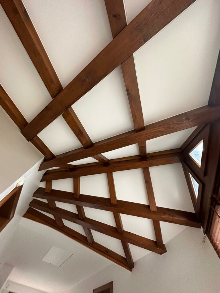 Plafond en bois avec poutres croisées et panneaux blancs dans une pièce lumineuse.