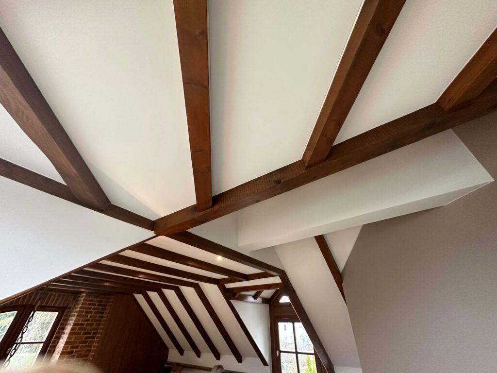 Plafond en bois avec poutres alignées et des angles modernes, éclairant un espace de vie.