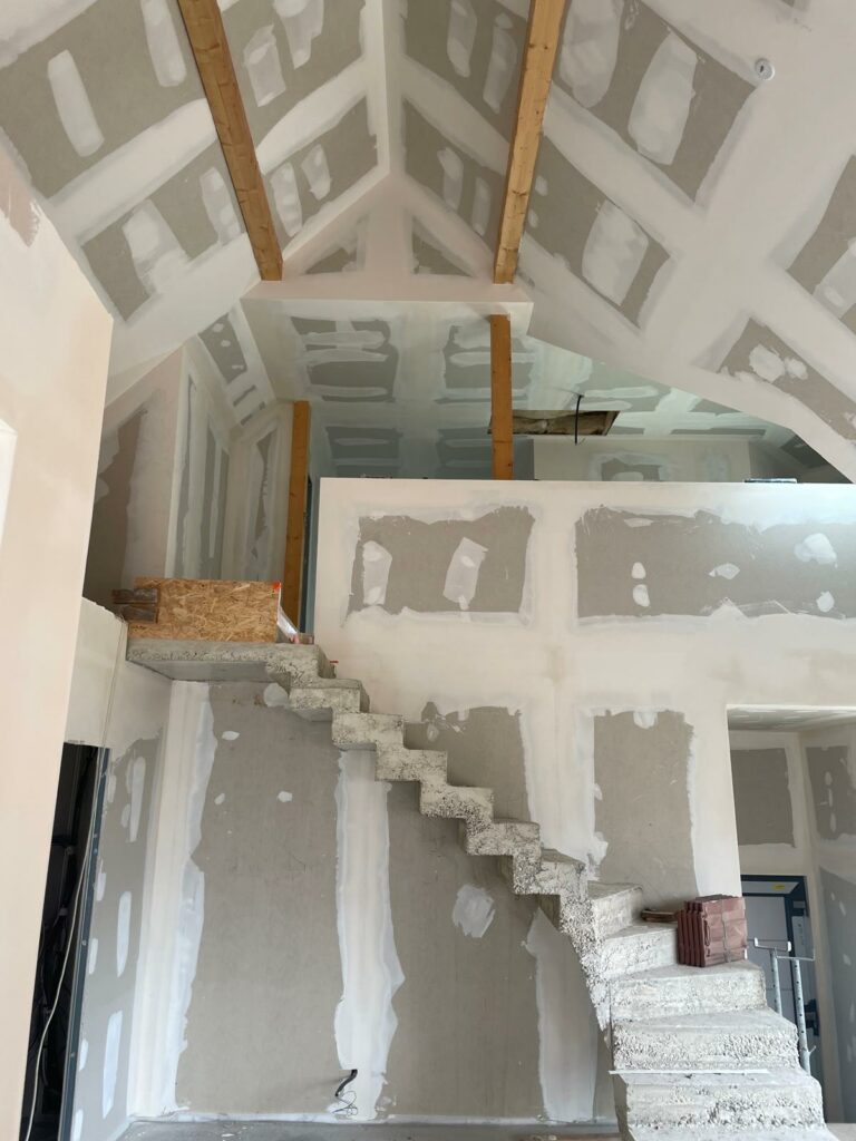 Intérieur spacieux avec un escalier en béton brut et des murs en plâtre en cours de finition.