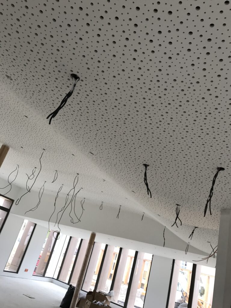 Plafond acoustique perforé en cours de finalisation, dans un espace lumineux avec de grandes fenêtres.