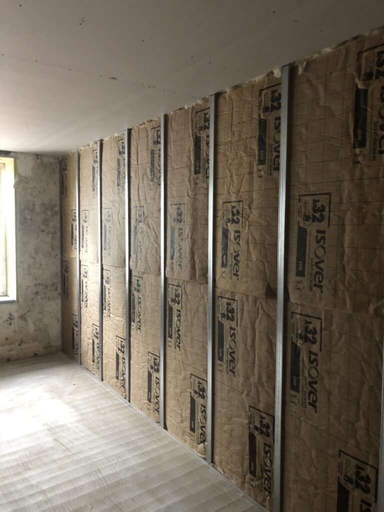 Cloison intérieure avec isolation acoustique en cours de réalisation, présentant une structure métallique et des panneaux isolants.