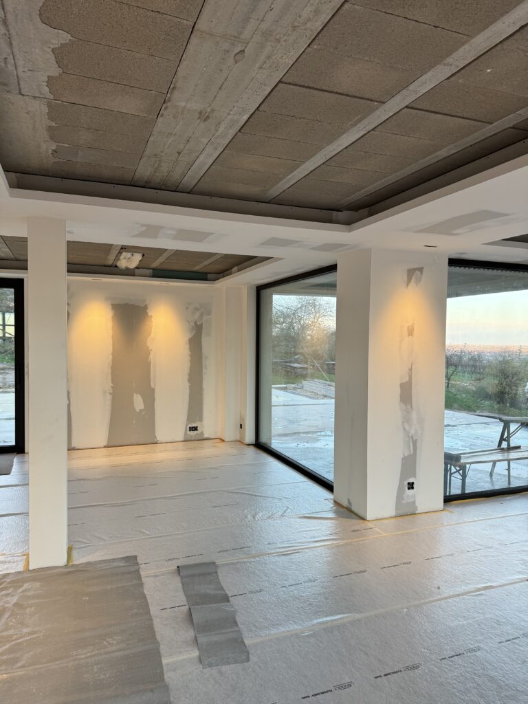 Espace de vie en cours de rénovation avec un faux plafond et des cloisons en préparation, offrant une vue lumineuse grâce à de grandes baies vitrées.