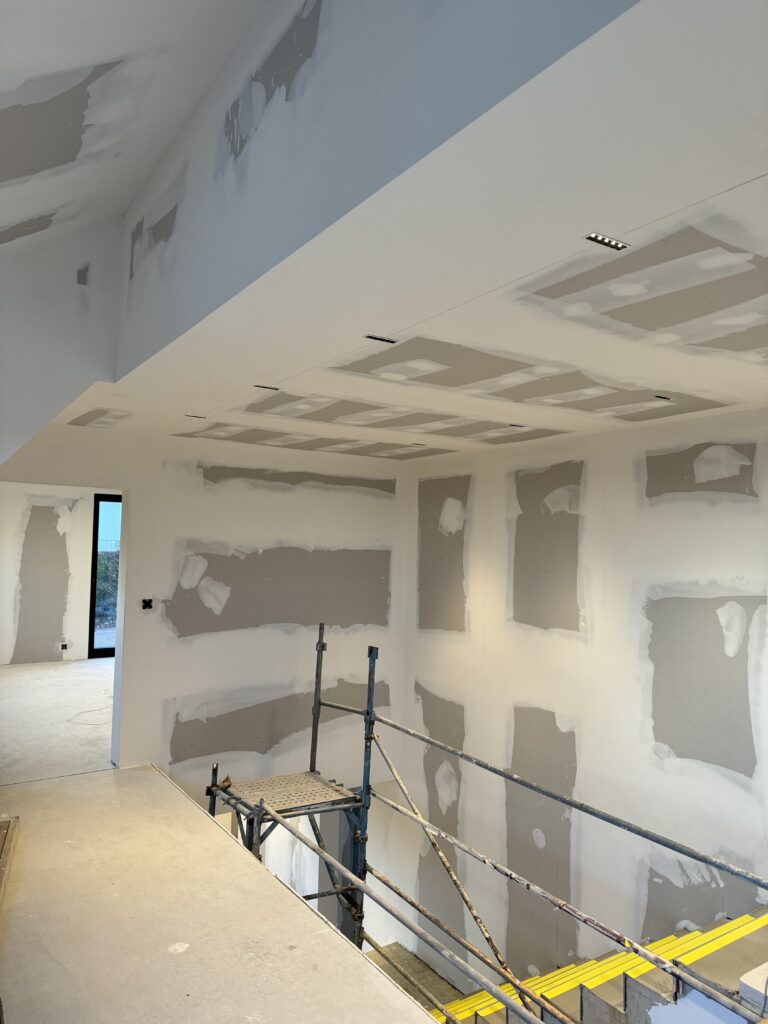 Vue intérieure d'un chantier avec un faux plafond complexe et des cloisons en plâtre en cours de finition, démontrant un savoir-faire de précision.