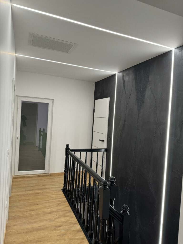 Couloir avec un faux plafond blanc et des lignes LED intégrées, combiné à des murs noirs texturés.