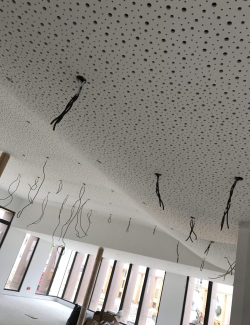 Plafond acoustique perforé en cours de finalisation, dans un espace lumineux avec de grandes fenêtres.