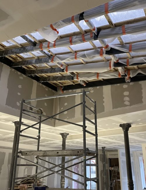 Charpente apparente en cours de couverture, avec des matériaux d'isolation sous un faux plafond.