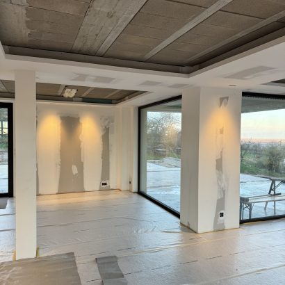 Espace de vie en cours de rénovation avec un faux plafond et des cloisons en préparation, offrant une vue lumineuse grâce à de grandes baies vitrées.
