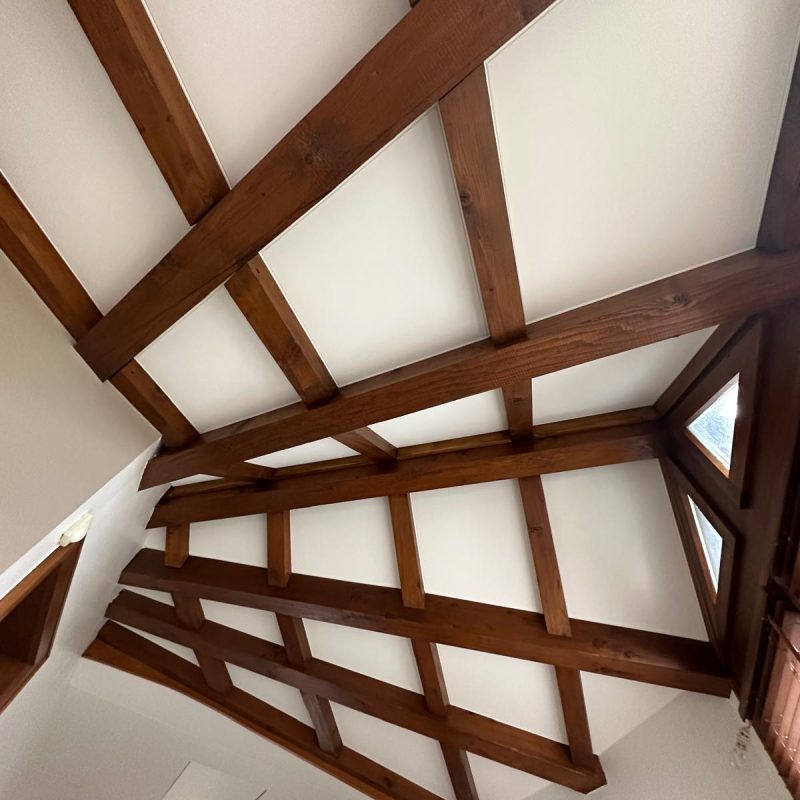 Plafond en bois avec poutres croisées et panneaux blancs dans une pièce lumineuse.