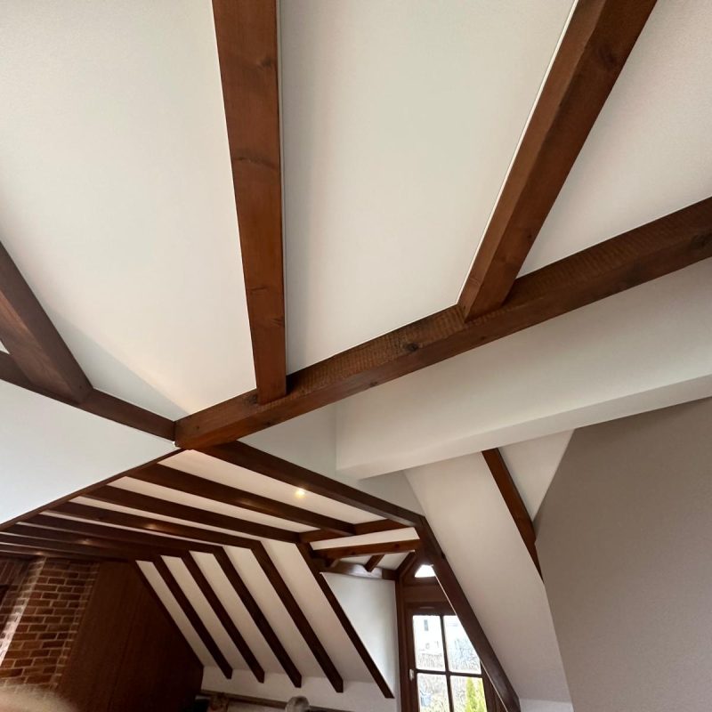 Plafond en bois avec poutres alignées et des angles modernes, éclairant un espace de vie.
