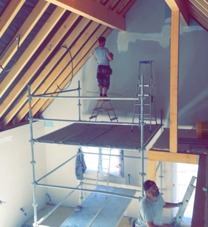 Artisans travaillant sur un échafaudage dans un espace avec charpente apparente.