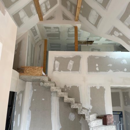 Intérieur spacieux avec un escalier en béton brut et des murs en plâtre en cours de finition.