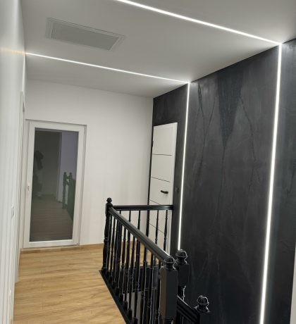Couloir avec un faux plafond blanc et des lignes LED intégrées, combiné à des murs noirs texturés.